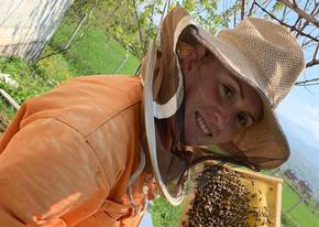 Shquipe Shala im Imkeranzug. Sie hält eine Wabe voller Bienen in der Hand und lacht.