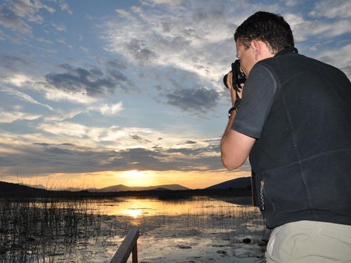 A man takes a photo of a sunset over a lake