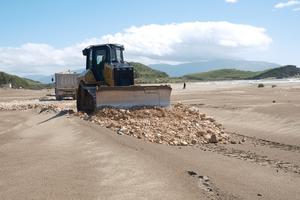 A bulldozer is piling up stones on the sandy beach