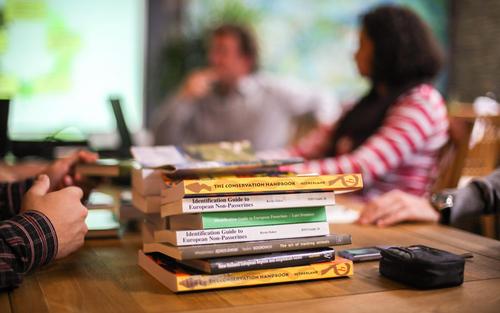 A pile of books lies on a meeting table.