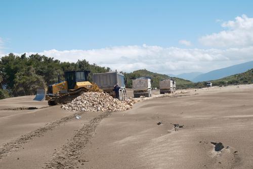 A road is being built in the sand; numerous lorries and a bulldozer can be seen.