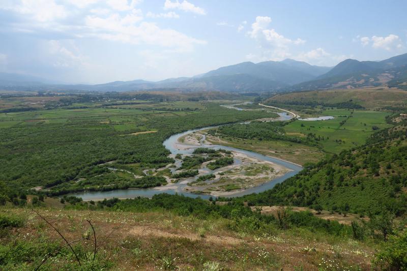 Blick von oben auf eine Flusslandschaft mit Feldern, Wiesen, Wäldern und Bergen.