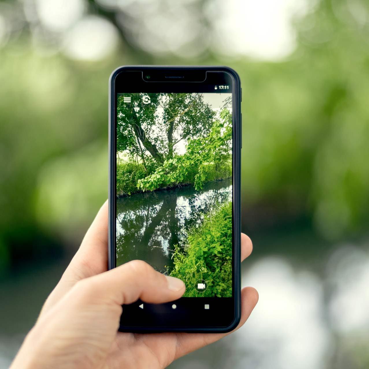 Der Bildschirm einses Smartphones, mit dem gerade ein Bach fotografiert wird.