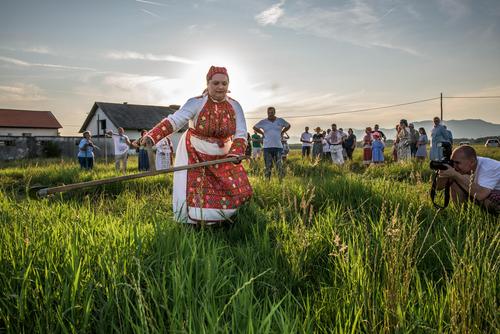 Eine Frau im traditionellen Kostüm mäht eine Wiese mit einer Sense.