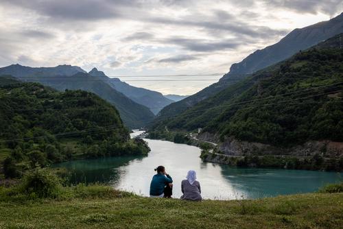 Zwei Frauen sitzen auf einer Wiese und schauen auf den Fluss hinunter.