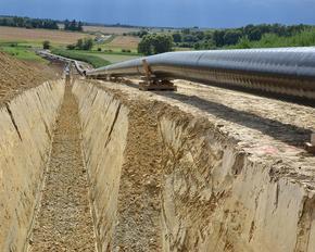 Baustelle für eine Erdgas-Pipeline. Ein tiefer Graben ist bereits ausgehoben, daneben liegen die zu verlegenden Rohre.