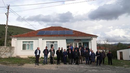 Menschen aus Kutë vor Gebäude mit Solarpaneel