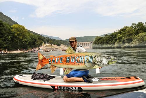 A stand-up paddler sits on his board and presents a poster in the shape of a huchen